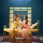 Tatsuo (Dai Tabuchi) wearing a khaki suit and sitting on a hospital bed with Yasuko (Phyllis Ho) and pointing.