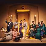 The cast of Disney's Hercules standing in the foyer of Theatre Royal Drury Lane with golden lighting around them.